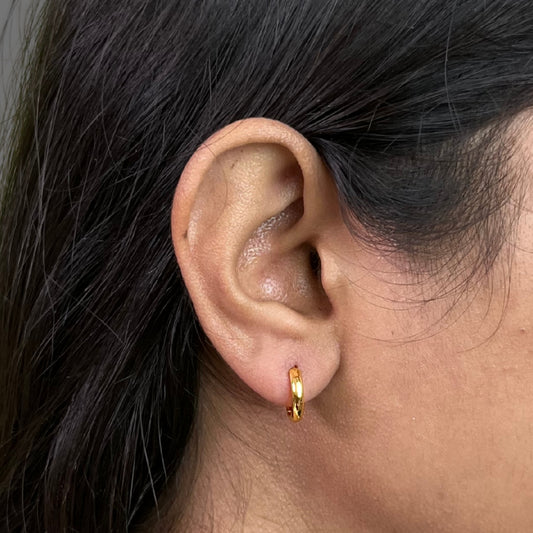 Close-up of an earring wearing a gold plated hoop earring with dark hair.