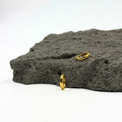 This image displays the Nira Kalyani Gold Plated Earrings, featuring a minimalist and elegant design. The earrings appear to be crafted from a lustrous gold material, shaped into sleek, loop-like structures.