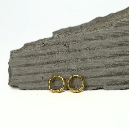 Nira Kalyani Gold plated hoops earrings on a textured gray surface